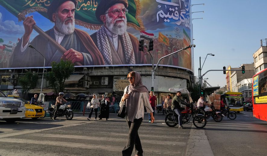 People walk under a banner showing portraits of the late revolutionary founder Ayatollah Khomeini, left, and the slain Supreme Leader Ayatollah Ali Khamenei, who was killed in U.S. and Israeli strikes on Feb. 28, in Tehran, Iran, Saturday, June 6, 2026. (AP Photo/Vahid Salemi)