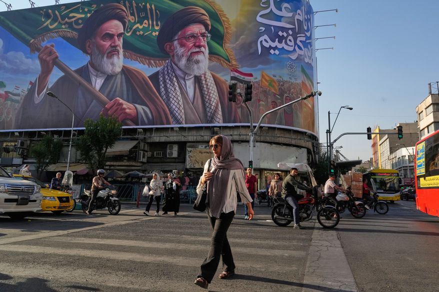 People walk under a banner showing portraits of the late revolutionary founder Ayatollah Khomeini, left, and the slain Supreme Leader Ayatollah Ali Khamenei, who was killed in U.S. and Israeli strikes on Feb. 28, in Tehran, Iran, Saturday, June 6, 2026. (AP Photo/Vahid Salemi)