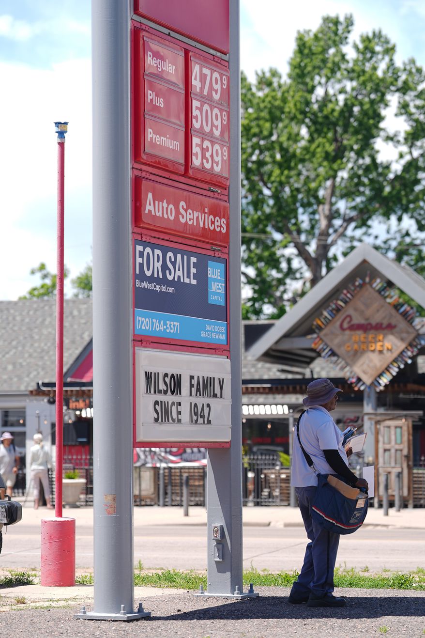 As the daytime high temperature soars into the 80s, a United States Postal Service postman keeps cool by standing in the shade of a gasoline station sign posting the per-gallon prices for the various grades of fuel available Thursday, June 4, 2026, in central Denver. (AP Photo/David Zalubowski)