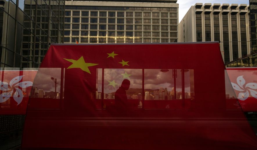 A pedestrian walks through a footbridge is silhouetted as Chinese and Hong Kong flags are strung to mark the 26th anniversary of the city's handover from Britain to China in Hong Kong, on June 27, 2023. (AP Photo/Louise Delmotte, File)