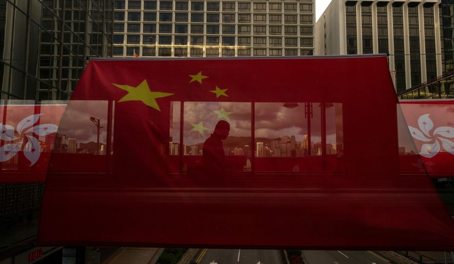 A pedestrian walks through a footbridge is silhouetted as Chinese and Hong Kong flags are strung to mark the 26th anniversary of the city's handover from Britain to China in Hong Kong, on June 27, 2023. (AP Photo/Louise Delmotte, File)