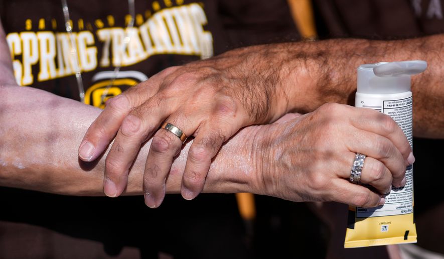 FILE - A man applies sunscreen to a woman's arm before a spring training baseball game between the San Diego Padres and the Chicago White Sox in Phoenix, Feb. 28, 2024. (AP Photo/Ashley Landis, File)