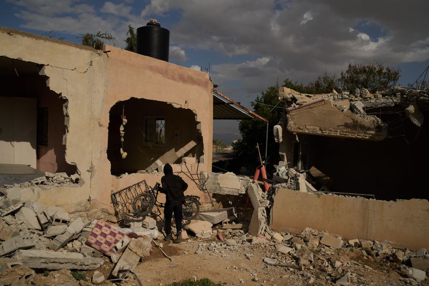 FILE -A Bedouin carries a bicycle past houses that, according to local residents, were heavily damaged yesterday during an attack by Israeli settlers in Al-Dyouk Al-Tahta area, on the outskirts of the West Bank city of Jericho, Feb. 11, 2026. (AP Photo/Leo Correa, File)