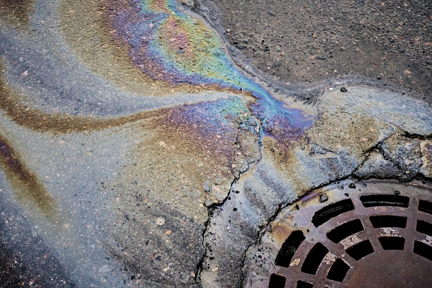 Oil slick on the asphalt road background drains into the storm drain. File photo credit: AlexFilim via Shutterstock.