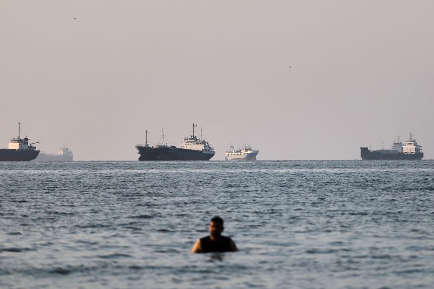 A person stands on shallow water as cargo and commercial vessels are anchored in the Strait of Hormuz off Bandar Abbas, Iran, Monday, June 8, 2026. (Amirhosein Khorgooi/ISNA via AP)