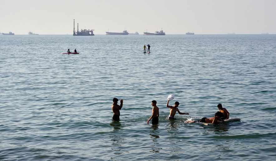 Residents swim and play in the waters of the Strait of Hormuz while cargo ships and commercial vessels lie anchored in the distance off Bandar Abbas, Iran, Wednesday, June 10, 2026.(Razieh Poudat/ISNA via AP)