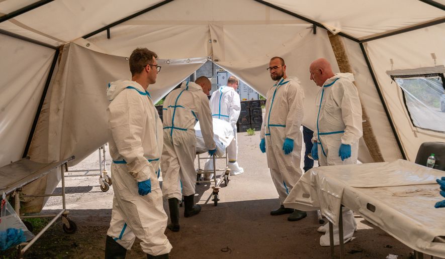 A dozen men in protective suits, surgical masks and latex gloves move between disaster-relief tents set up alongside the rail cars in Odesa, Ukraine, as they try to identify Ukraine's war fatalities. (Marie Montels/Special to The Washington Times)