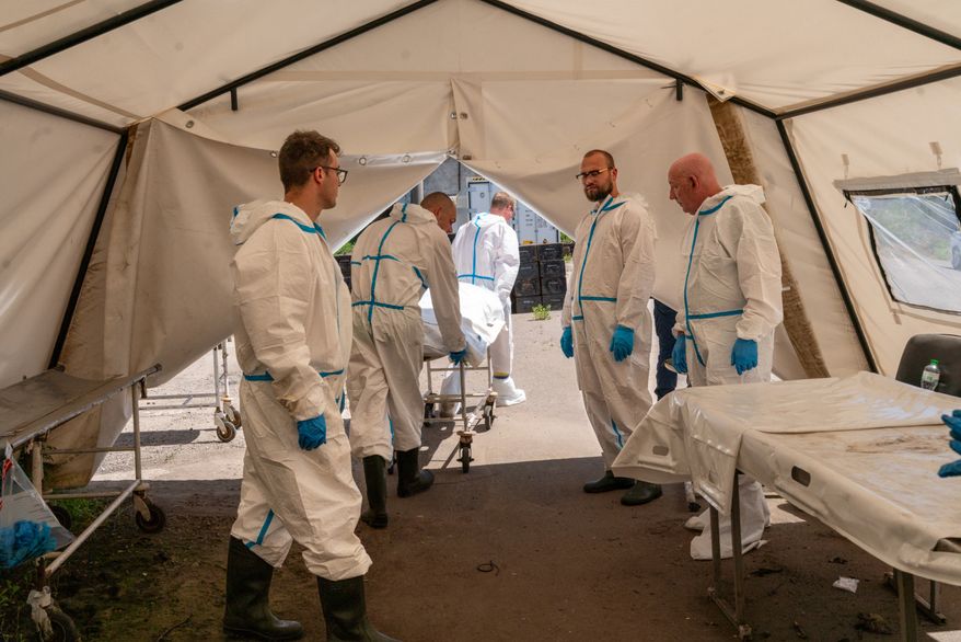 A dozen men in protective suits, surgical masks and latex gloves move between disaster-relief tents set up alongside the rail cars in Odesa, Ukraine, as they try to identify Ukraine's war fatalities. (Marie Montels/Special to The Washington Times)