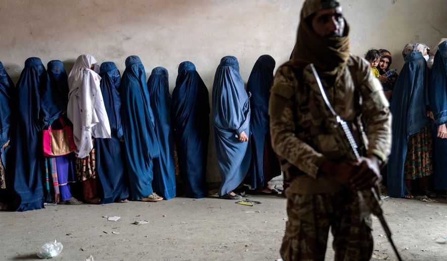 FILE - A Taliban fighter stands guard as women wait to receive food rations distributed by a humanitarian aid group, in Kabul, Afghanistan, Tuesday, May 23, 2023. (AP Photo/Ebrahim Noroozi, file)