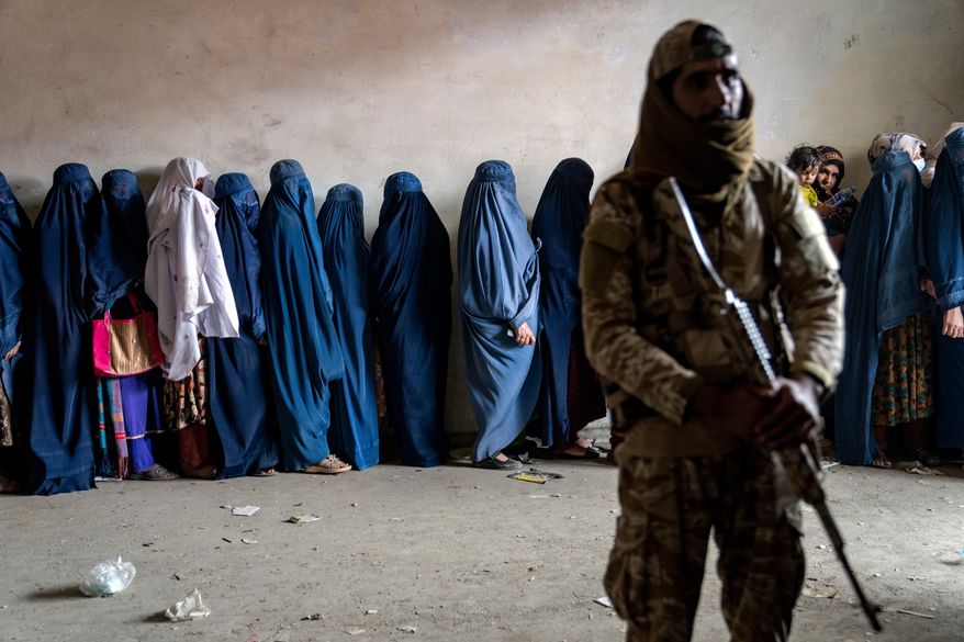 FILE - A Taliban fighter stands guard as women wait to receive food rations distributed by a humanitarian aid group, in Kabul, Afghanistan, Tuesday, May 23, 2023. (AP Photo/Ebrahim Noroozi, file)