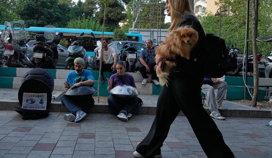 Street musicians play music as a woman carries a dog on a sidewalk in northern Tehran, Wednesday, June 10, 2026. (AP Photo/Vahid Salemi)
