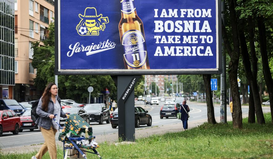 A woman walks past a billboard displaying lyrics from the Dubioza kolektiv song "I Am From Bosnia, Take Me to America" in Sarajevo, Bosnia, Thursday, June 11, 2026. (AP Photo/Armin Durgut)