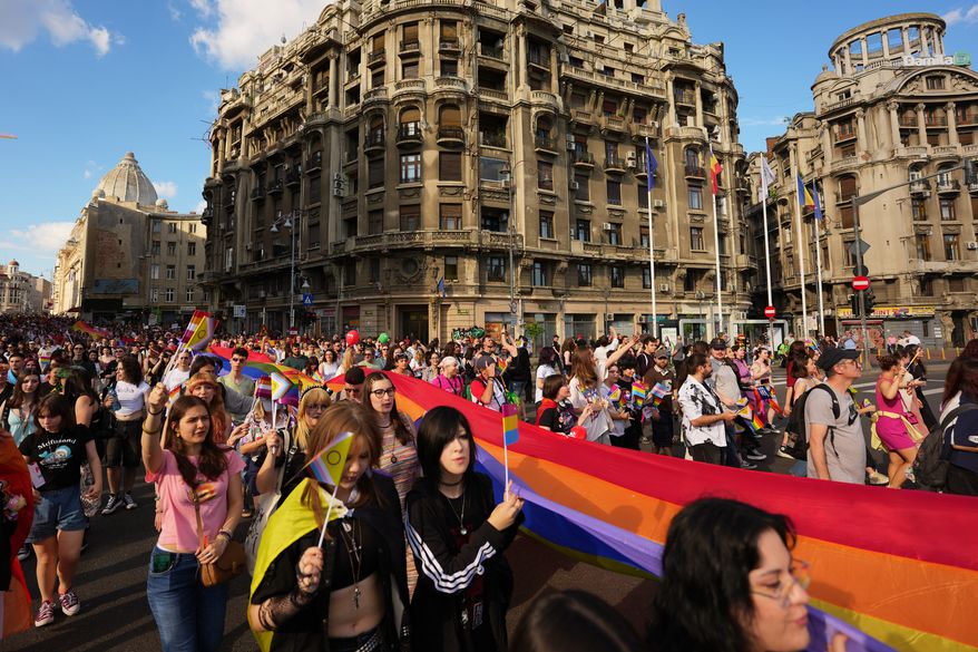 People walk carrying a rainbow flag during the Bucharest Pride Parade, in Bucharest, Romania, Saturday, June 13, 2026. (AP Photo/Andreea Alexandru)
