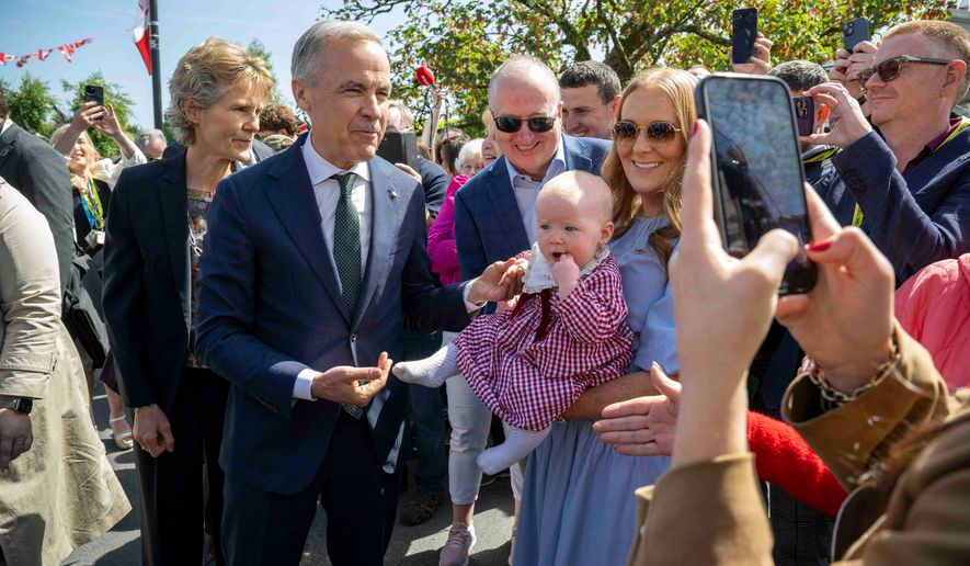 Canadian Prime Minister Mark Carney, front left, has a picture taken with Lily Meskil, 9 months and her grandfather Ger Basquel and mother Rachel Basquel, during a visit to Aughagower, Ireland, Sunday, June 14, 2026. (Andrew Downes/PA via AP)