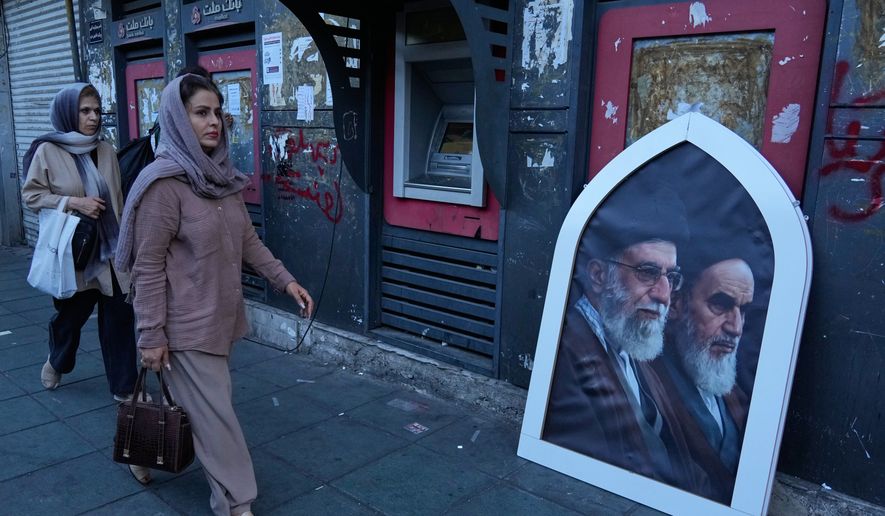 Pedestrians walk past a poster showing the slain Iranian Supreme Leader Ayatollah Ali Khamenei, left, and the late revolutionary founder Ayatollah Khomeini on a sidewalk at the Islamic Revolution square in Tehran, Iran, Sunday, June 14, 2026. (AP Photo/Vahid Salemi)