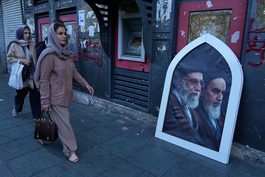 Pedestrians walk past a poster showing the slain Iranian Supreme Leader Ayatollah Ali Khamenei, left, and the late revolutionary founder Ayatollah Khomeini on a sidewalk at the Islamic Revolution square in Tehran, Iran, Sunday, June 14, 2026. (AP Photo/Vahid Salemi)