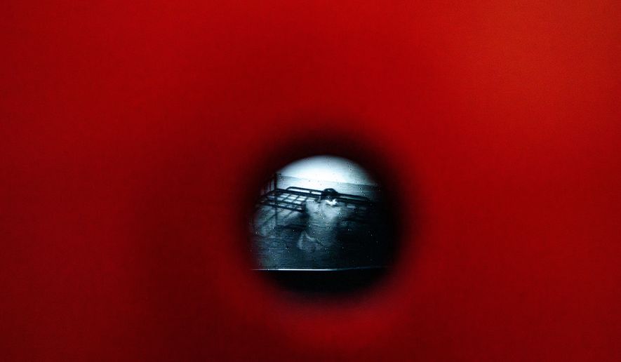 A video from the Communist era secret police surveillance archives, seen through a pinhole, shows Anton Uncu sitting on a metal bed, a day before the opening of the "A.REST 1989 — The Securitate Video Archive" exhibition, at the National History Museum of Romania, in Bucharest, Romania, Monday, June 15, 2026. (AP Photo/Andreea Alexandru)