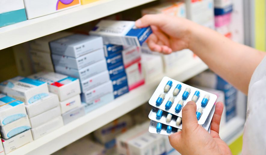 Pharmacist holding medicine box and capsule pack in pharmacy drugstore. File photo credit: i viewfinder via Shutterstock.