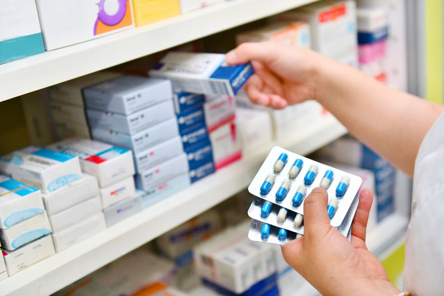 Pharmacist holding medicine box and capsule pack in pharmacy drugstore. File photo credit: i viewfinder via Shutterstock.