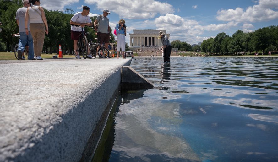 Visitors watch as a National Park Service employee uses a vacuum to clean the Lincoln Memorial Reflecting Pool near a missing section of blue coating, Friday, June 19, 2026, in Washington. (AP Photo/Mark Schiefelbein)