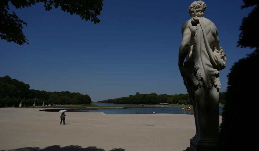 A woman shields herself from the sun with an umbrella as she walks in the garden of the Palace of Versailles, outside Paris, during a heat wave with temperatures soaring above 40 degrees Celsius (104 Fahrenheit), Monday, June 22, 2026. (AP Photo/Thibault Camus)