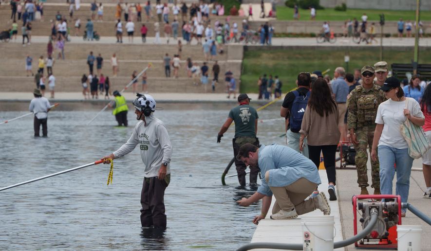 A visor takes a photo as National Park Service employees work to clean the Lincoln Memorial Reflecting Pool Sunday, June 21, 2026, on the National Mall in Washington. (AP Photo/Jon Elswick