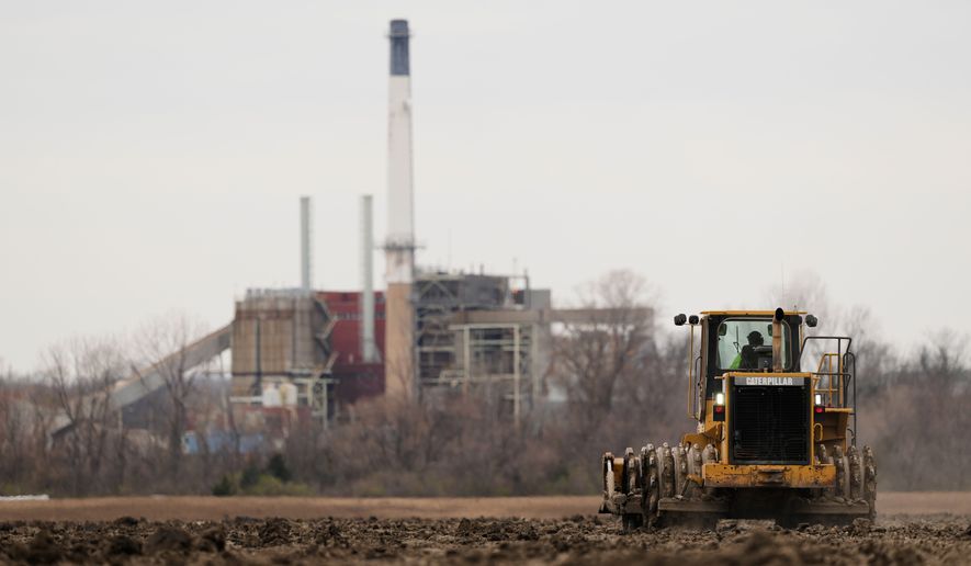 A worker prepares a plot of land for an AI data center, with a retired power plant being refurbished to provide electricity for the facility in the distance, March 24, 2026, in Independence, Mo. (File, AP Photo/Charlie Riedel)