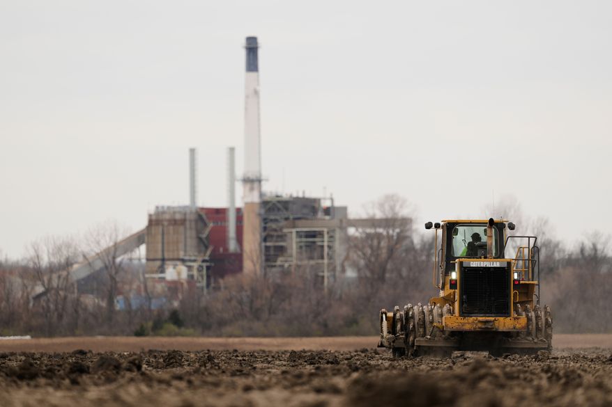 A worker prepares a plot of land for an AI data center, with a retired power plant being refurbished to provide electricity for the facility in the distance, March 24, 2026, in Independence, Mo. (File, AP Photo/Charlie Riedel)