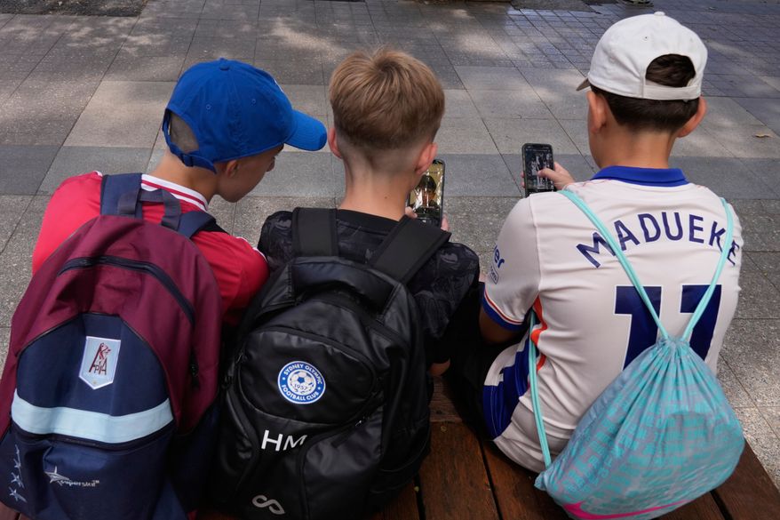 FILE - Three boys use their phones while sitting outside a school in Sydney, Monday, Dec. 8, 2025. (AP Photo/Rick Rycroft, File)