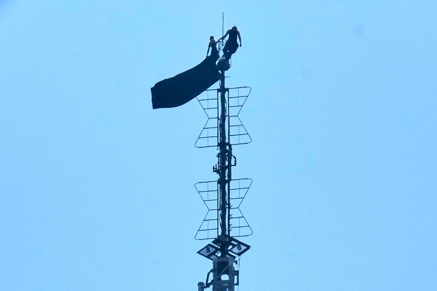 Two people stand on the tip of the antenna of the Empire State Building while holding a banner on Wednesday, July 1, 2026. (AP Photo/Richard Drew)