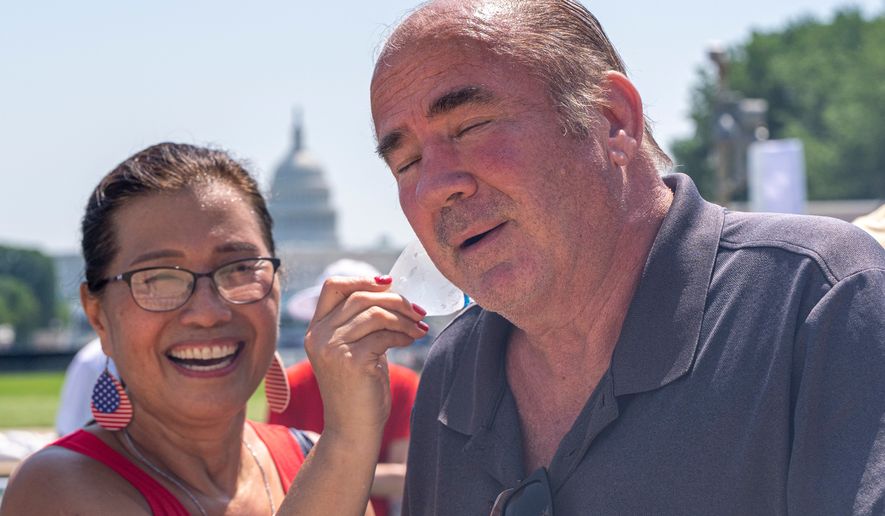 Stephanie McCallister holds a cold bottle of water to her husband Don McCallister's neck as they wait in line for the ferris wheel at the Great American State Fair on the National Mall, Wednesday, July 1, 2026, in Washington. (AP Photo/Jen Golbeck)