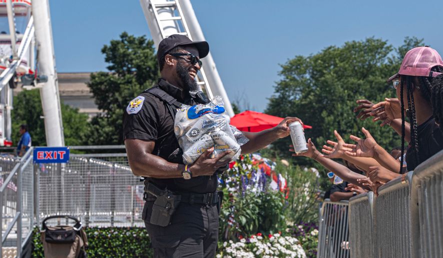 Children reach for cold bottles of water from U.S. National Park Police Officer R. Douglass as they wait in line for the ferris wheel at the Great American State Fair on the National Mall, Wednesday, July 1, 2026, in Washington. (AP Photo/Jen Golbeck)