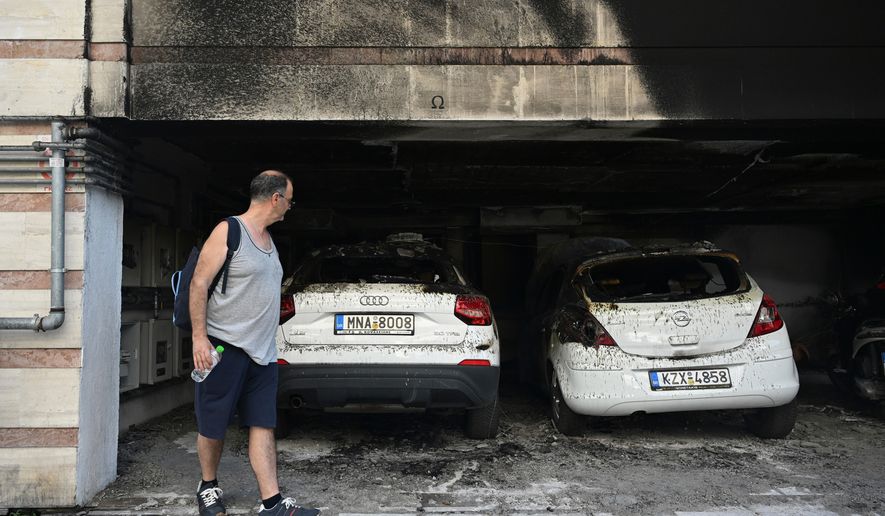 A man looks at burned vehicles following firebomb attacks that apparently targeted members of Greece's governing conservative New Democracy party in the northern port city of Thessaloniki, Greece, Wednesday, July 1, 2026. (AP Photo/Giannis Papanikos)