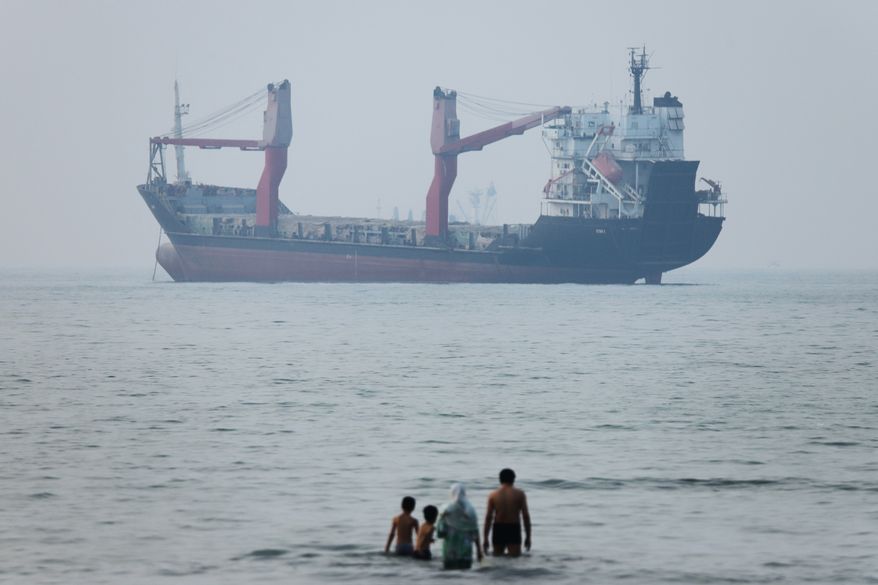 A group of people stands in shallow water as a cargo ship appears anchored in the Strait of Hormuz off Bandar Abbas, Iran, Tuesday, June 30, 2026. (Amirhosein Khorgooi/ISNA via AP)