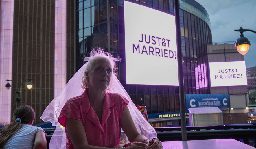 A Taylor Swift fan wearing a wedding veil sits at a restaurant next to Madison Square Garden where a "JUST&T MARRIED" sign is displayed during a wedding between singer Taylor Swift and National Football League player Travis Kelce on Friday, July 3, 2026, in New York. (AP Photo/Ryan Murphy)