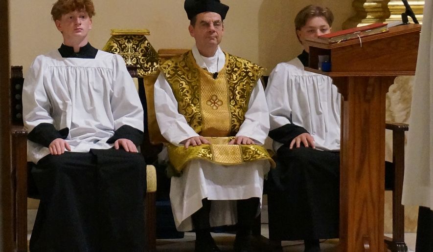 The Rev. John Ubel, pastor of the Church of Saint Agnes, wears the traditional biretta hat and vestments as he sits between altar servers during one of the Catholic parish’s Latin Masses in St. Paul, Minn., Sunday, June 28, 2026. (AP Photo/Giovanna Dell’Orto)