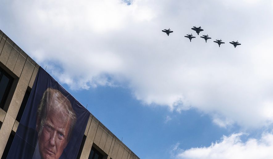 A flight of F-18s, F-35s and a F-22 fly past a picture of President Donald Trump hanging on the U.S. Department of Labor near the Great American State Fair on the National Mall, Friday, July 3, 2026, in Washington. (AP Photo/Nathan Howard)