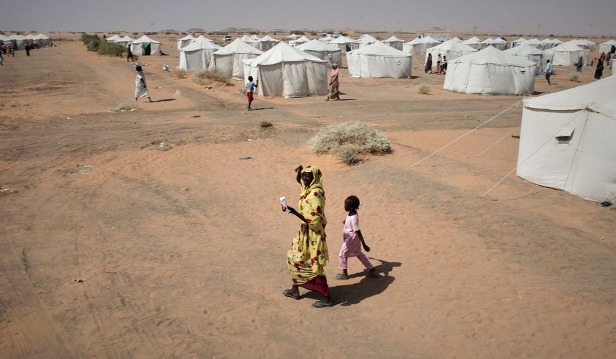 FILE - A woman and a child, displaced from North Darfur's capital, el-Fasher or other conflict-affected areas walk in the newly established El-Afadh camp in Al Dabbah, in Sudan's Northern State, Sudan, Thursday, Nov. 13, 2025. (AP Photo/Marwan Ali, File)