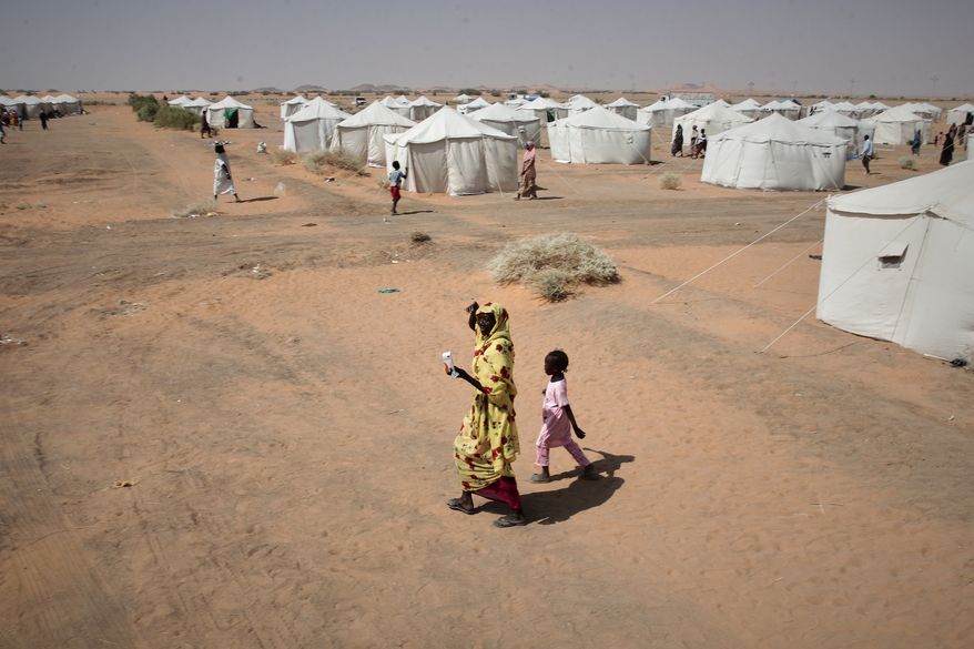 FILE - A woman and a child, displaced from North Darfur's capital, el-Fasher or other conflict-affected areas walk in the newly established El-Afadh camp in Al Dabbah, in Sudan's Northern State, Sudan, Thursday, Nov. 13, 2025. (AP Photo/Marwan Ali, File)