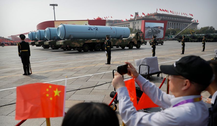 Spectators wave Chinese flags as military vehicles carrying JL-2 submarine-launched missiles roll during a parade to commemorate the 70th anniversary of the founding of Communist China in Beijing, Oct. 1, 2019. (AP Photo/Mark Schiefelbein, File)