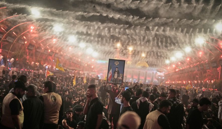 A mourner holds a portrait depicting Iran's Supreme Leader Ayatollah Mojtaba Khamenei, top, and his late father, Ayatollah Ali Khamenei, as mourners wait for the funeral procession for the elder Khamenei outside the Imam Hussein Shrine in Karbala, Iraq, Wednesday, July 8, 2026. (AP Photo/Khalil Hamra)