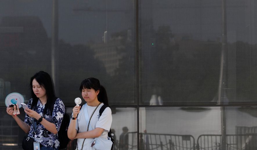 Visitors use fans as as they wait to enter the Washington Monument, July 1, 2026, in Washington. (AP Photo/Tom Brenner, File)