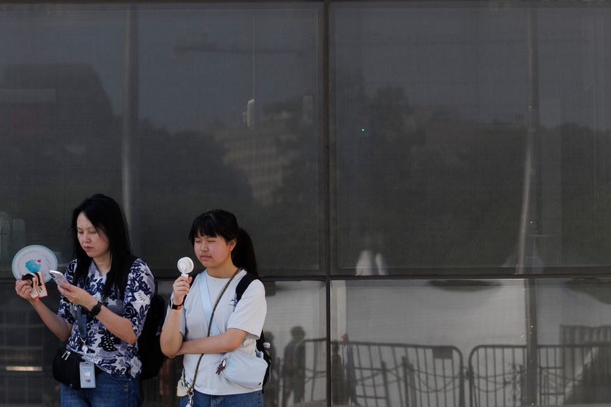 Visitors use fans as as they wait to enter the Washington Monument, July 1, 2026, in Washington. (AP Photo/Tom Brenner, File)