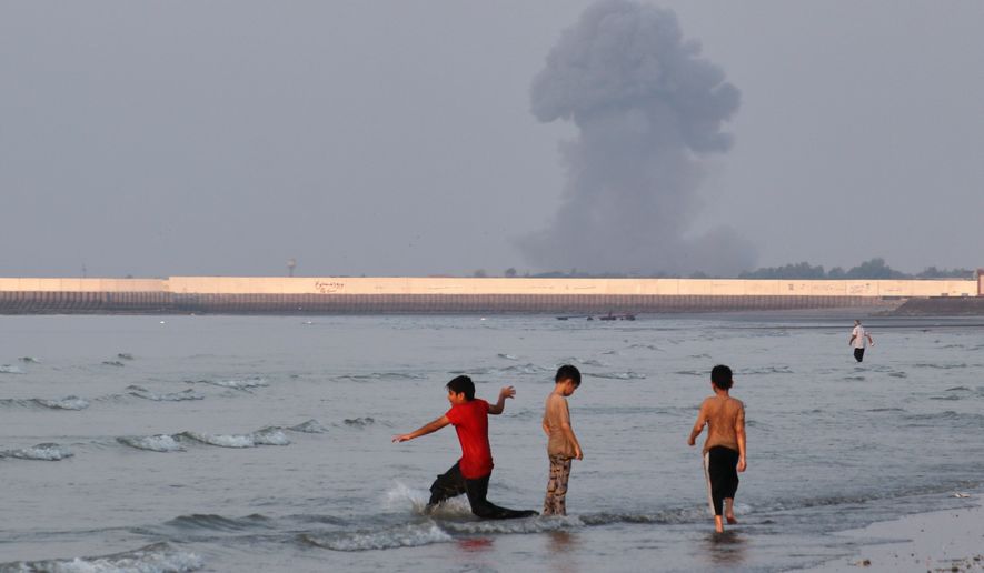 Three boys play in the shallow waters of the Strait of Hormuz, as a plume of smoke rises from an explosion in the background, off Bandar Abbas, Iran, Monday, July 13, 2026. (Razieh Poudat/ISNA via AP)