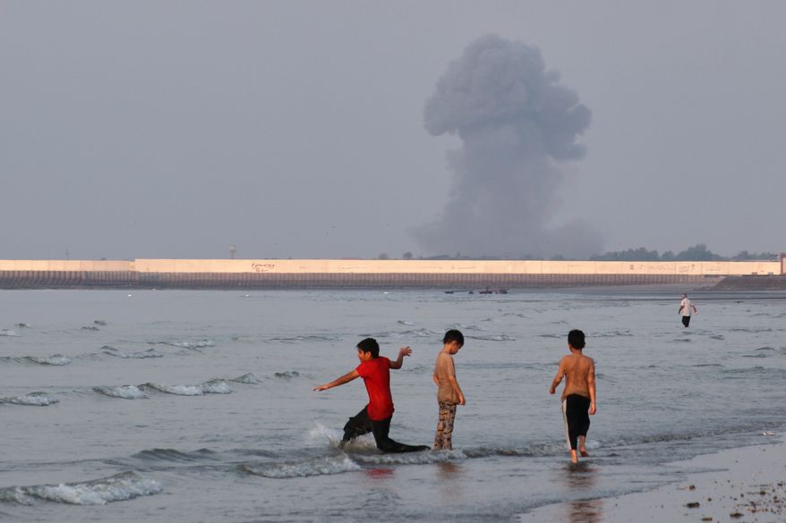 Three boys play in the shallow waters of the Strait of Hormuz, as a plume of smoke rises from an explosion in the background, off Bandar Abbas, Iran, Monday, July 13, 2026. (Razieh Poudat/ISNA via AP)