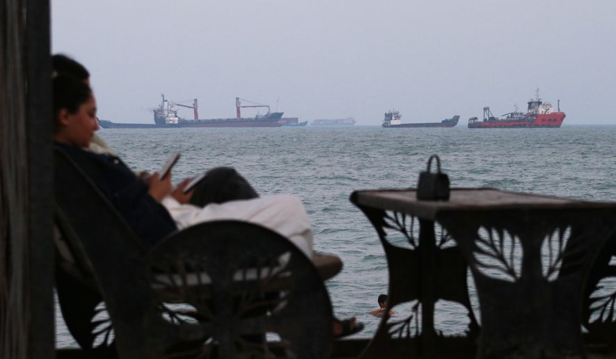 Residents check their cellphones as they sit at a cafe overlooking commercial vessels anchored in the Strait of Hormuz, off Bandar Abbas, Iran, Sunday, July 12, 2026. (Razieh Poudat/ISNA via AP)