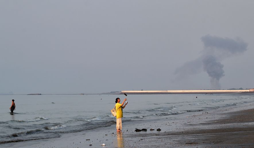 A woman stands at the water's edge along the Strait of Hormuz as a plume of smoke rises in the background following an explosion, off Bandar Abbas, Iran, Monday, July 13, 2026. (Razieh Poudat/ISNA via AP)
