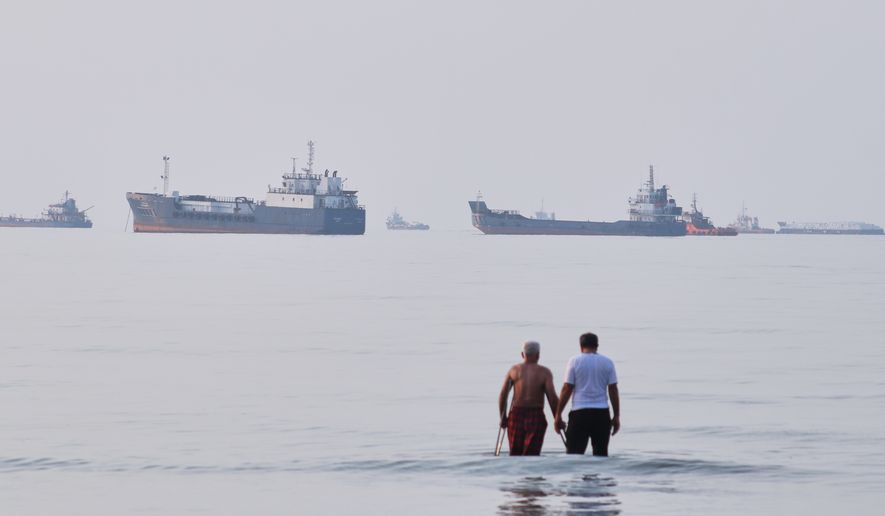 Two men wade in the waters of the Strait of Hormuz with vessels anchored in the background, off Bandar Abbas, Iran, Sunday, July 12, 2026. (Razieh Poudat/ISNA via AP)