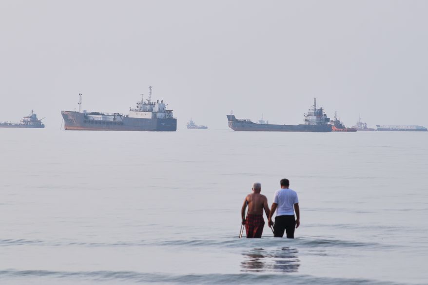 Two men wade in the waters of the Strait of Hormuz with vessels anchored in the background, off Bandar Abbas, Iran, Sunday, July 12, 2026. (Razieh Poudat/ISNA via AP)