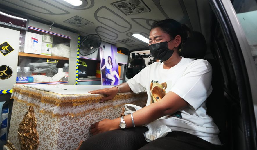 A relative of a victim in a music bar fire sits near the coffin containing the victim's body inside a vehicle as it is transferred from a police hospital in Bangkok, Thailand, Wednesday, July 15, 2026, (AP Photo/Sakchai Lalit)